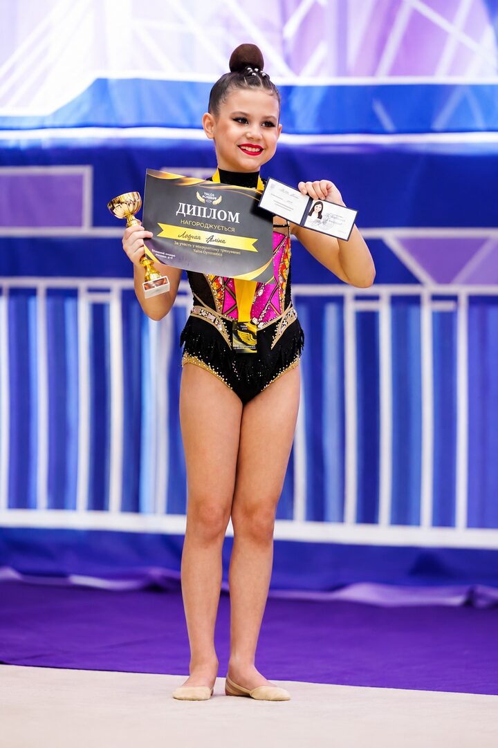 A young YALOS gymnast with her diploma, trophy and certificate at a competition