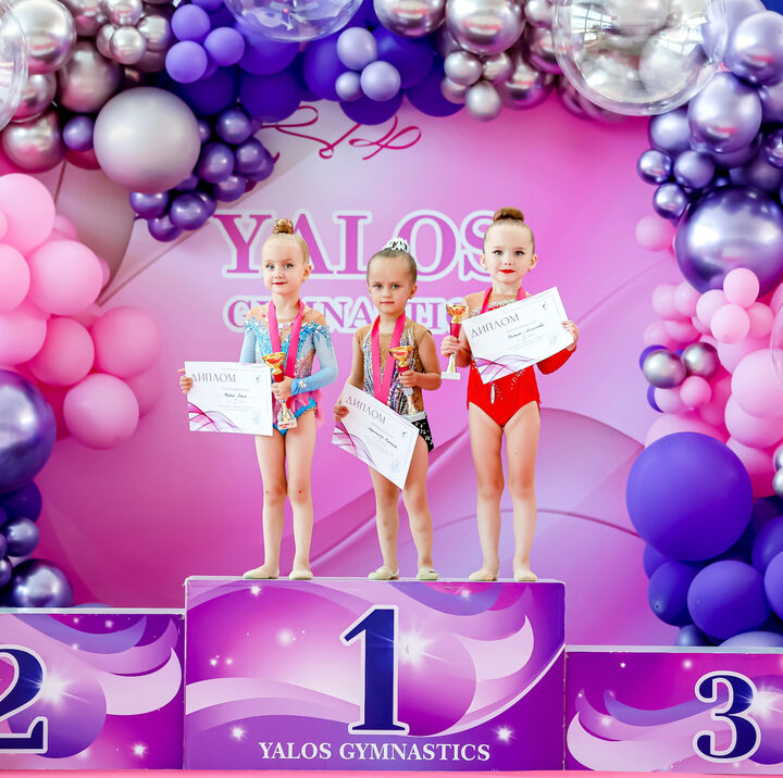 Young YALOS gymnasts on the podium with diplomas and trophies